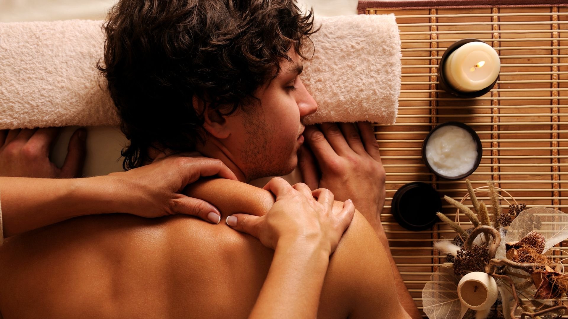 Person receiving relaxing massage at spa with candles and bamboo backdrop